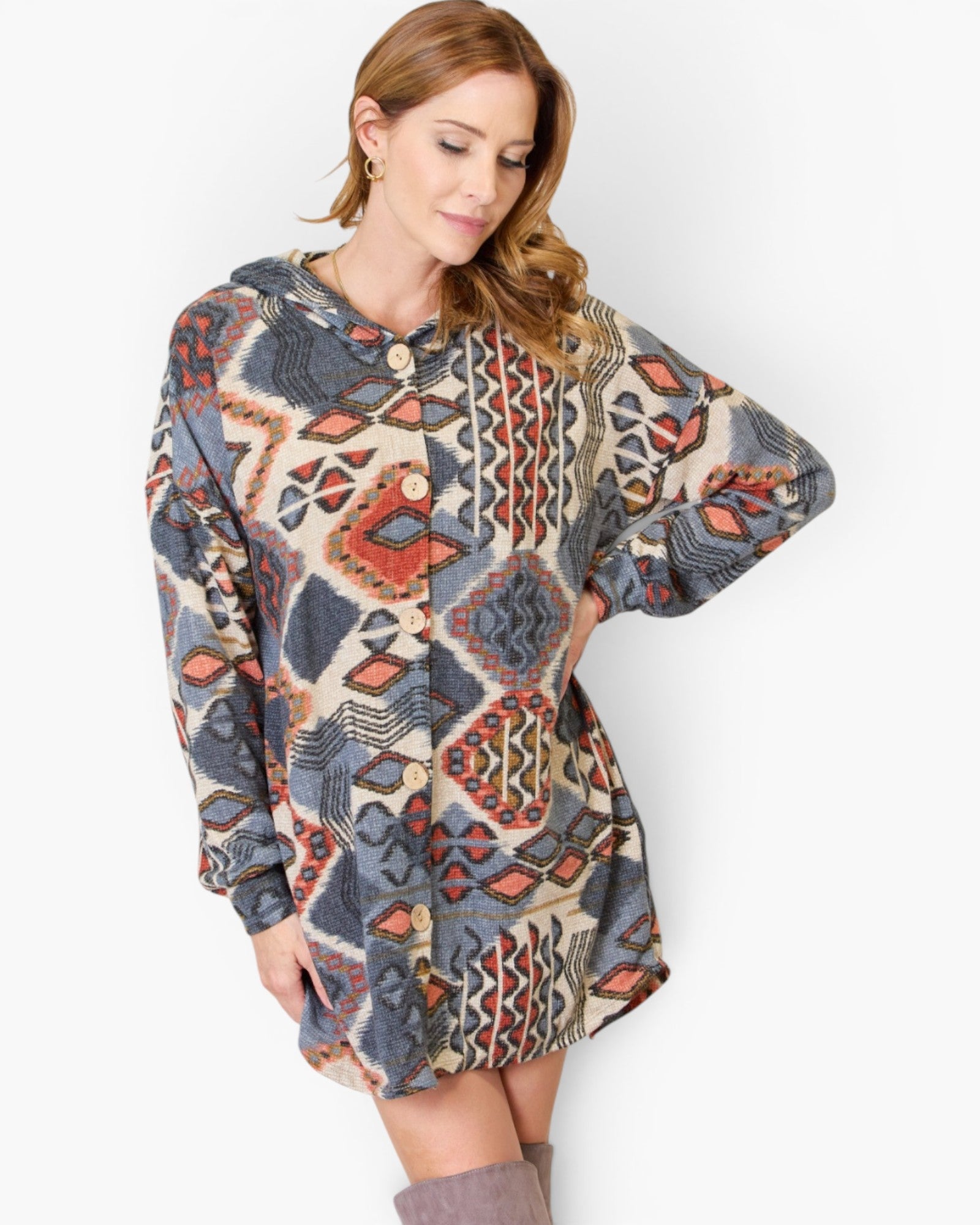 A woman wearing a long-sleeve button-front hooded dress with an all-over geometric pattern in beige, blue, red, and orange, posed against a plain light gray studio background.