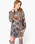 A woman wearing a long-sleeve button-front dress with a colorful geometric tribal pattern in blue, red, orange, and beige, paired with gray over-the-knee boots, against a light gray background.