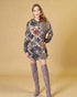 Woman wearing a patterned dress and gray knee-high boots against a beige background
