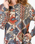 A close-up of a woman wearing a long-sleeve button-front top with an intricate geometric tribal pattern in blue, red, orange, and beige.