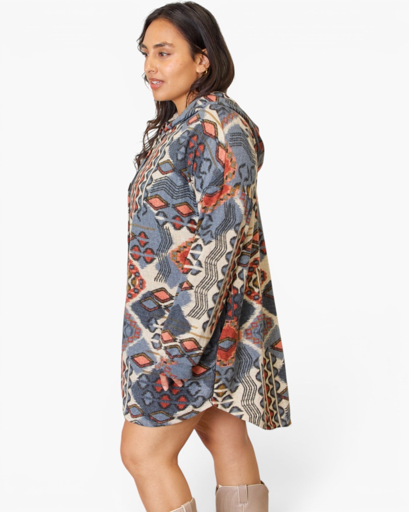 A woman wearing a loose, knee-length hooded tunic dress with an abstract geometric pattern in beige, slate blue, rust orange, and black, shown from a side-back angle against a plain white studio background.