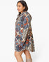A woman wearing a loose, knee-length hooded tunic dress with an abstract geometric pattern in beige, slate blue, rust orange, and black, shown from a side-back angle against a plain white studio background.
