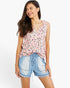 A woman modeling a sleeveless pink leopard-print top and light-wash denim shorts against a plain white studio background.