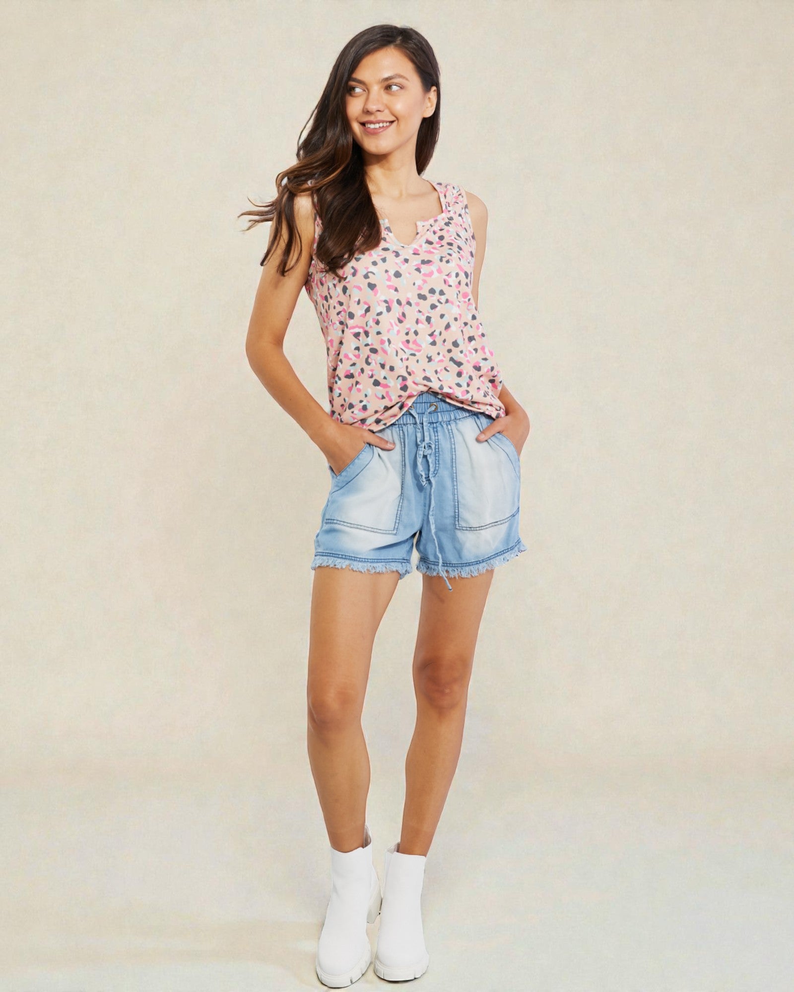 Woman wearing a floral tank top and denim shorts against a plain background