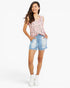 A woman modeling a sleeveless pink floral top and light blue denim shorts against a plain white studio background.