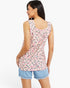 A woman shown from the back wearing a sleeveless scoop-neck tank top with a pink, black, and green abstract print on a light beige background, paired with light blue denim shorts.