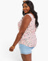 A woman modeling a sleeveless wrap-style top with a pink, black, and gray leopard print on a white background, paired with light blue denim shorts, against a plain white studio background.