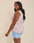 Woman wearing a sleeveless floral top and denim shorts on a beige background