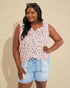 Woman wearing a sleeveless floral top and denim shorts against a beige background
