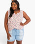 A plus-size woman modeling a sleeveless scoop-neck top with a pink, gray, and black leopard print on a light pink background, paired with light-wash denim shorts against a white studio background.