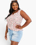 A woman modeling a sleeveless V-neck top with a pink, gray, and black leopard print pattern, paired with light blue denim shorts, against a plain white background.