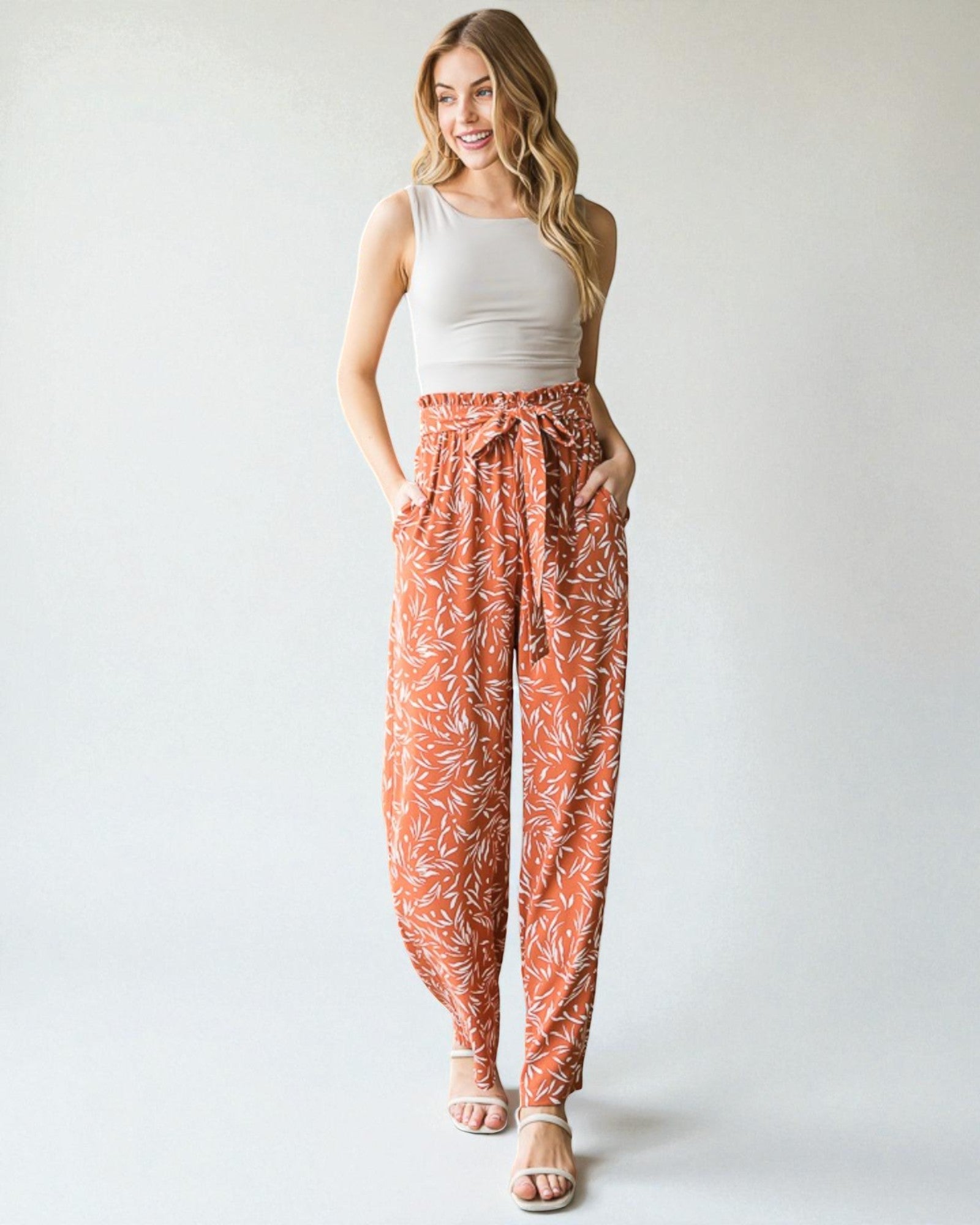Woman wearing a white tank top and orange patterned pants on a plain background