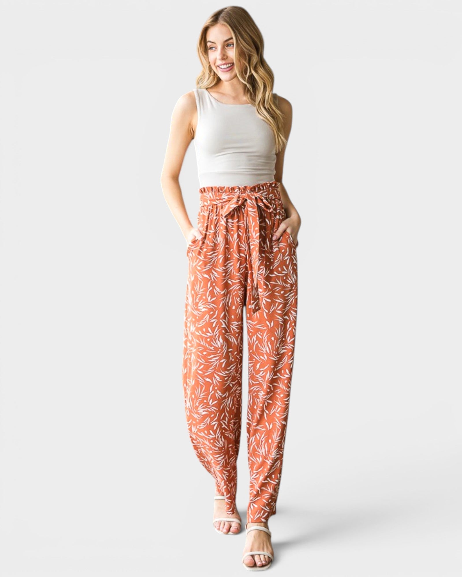 Woman wearing a white tank top and orange floral pants on a white background