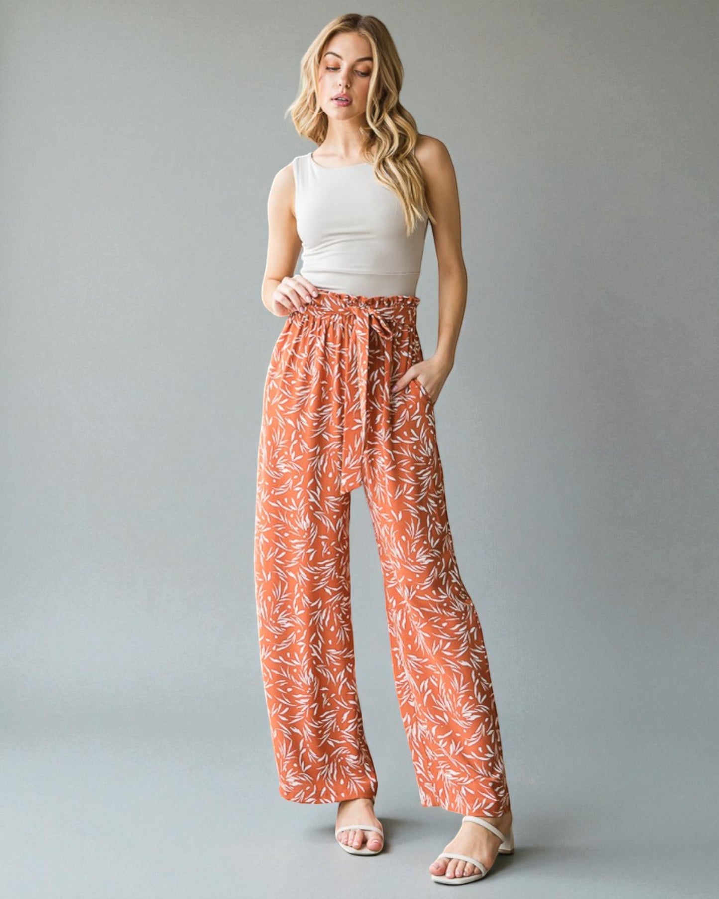 Woman wearing a white top and orange patterned pants on a gray background