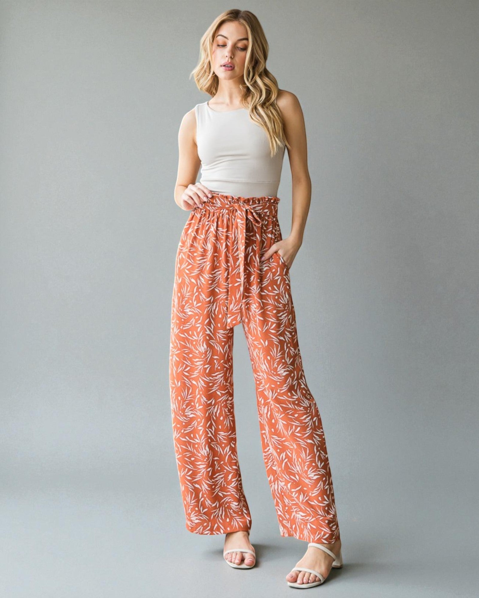 Woman wearing a white top and orange patterned pants on a gray background