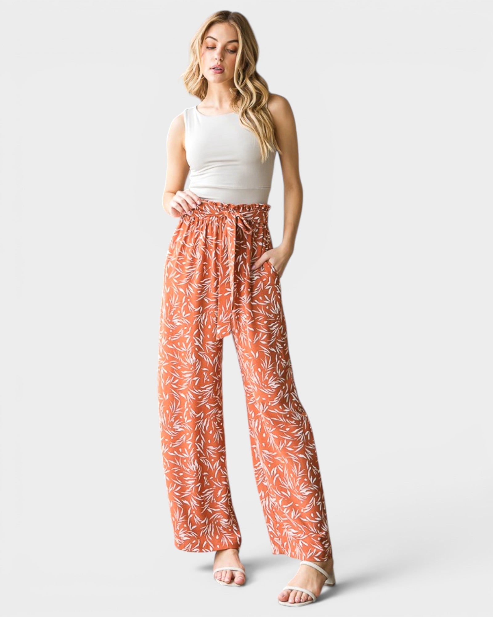 Woman wearing a white tank top and orange floral pants on a light gray background