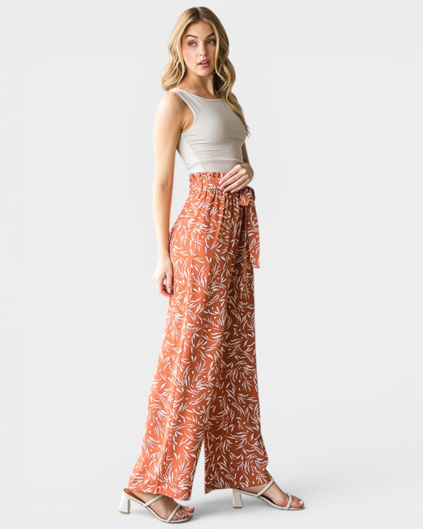 Woman wearing a white top and orange patterned pants on a white background