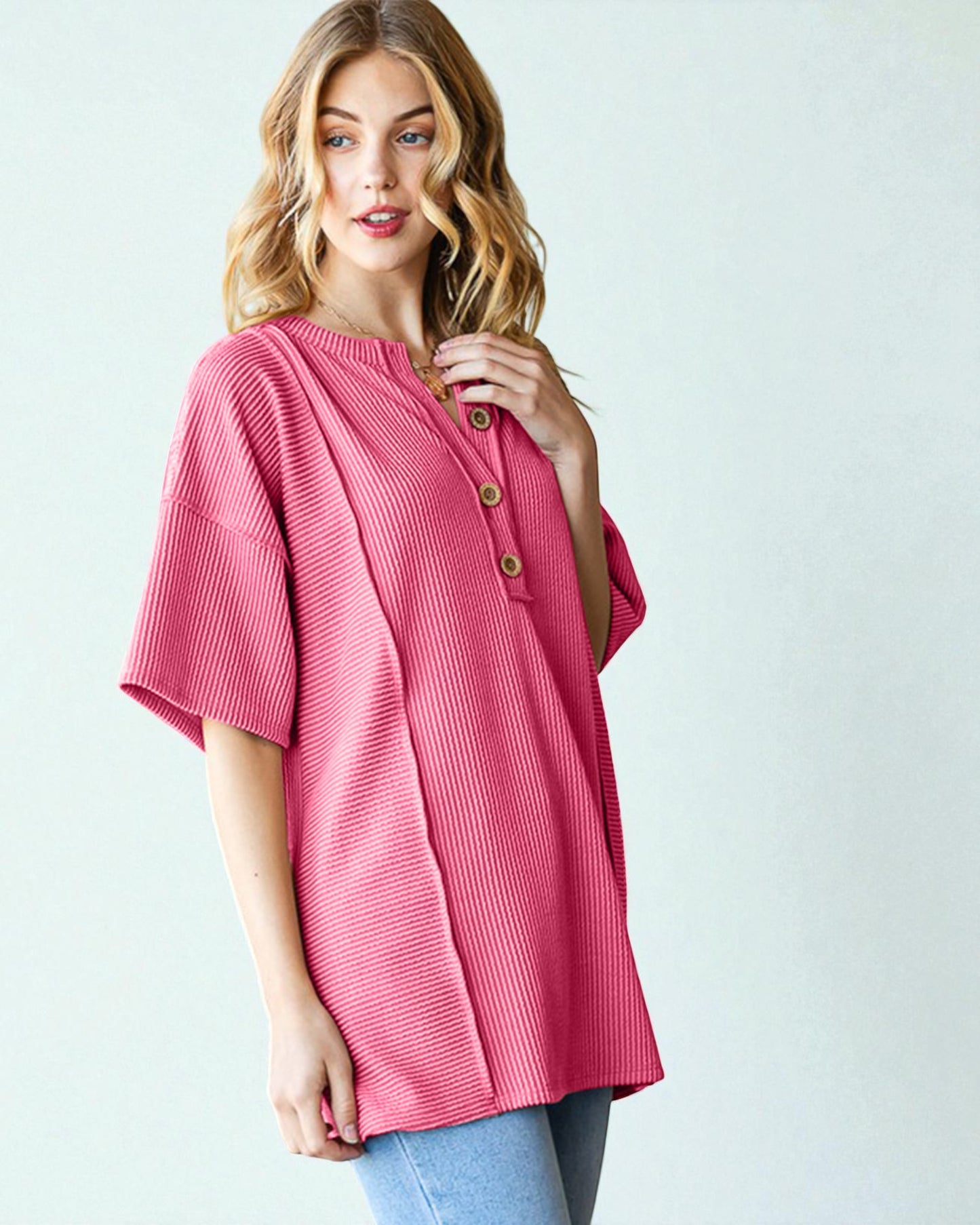 Woman wearing a pink ribbed sweater with button details on a light gray background