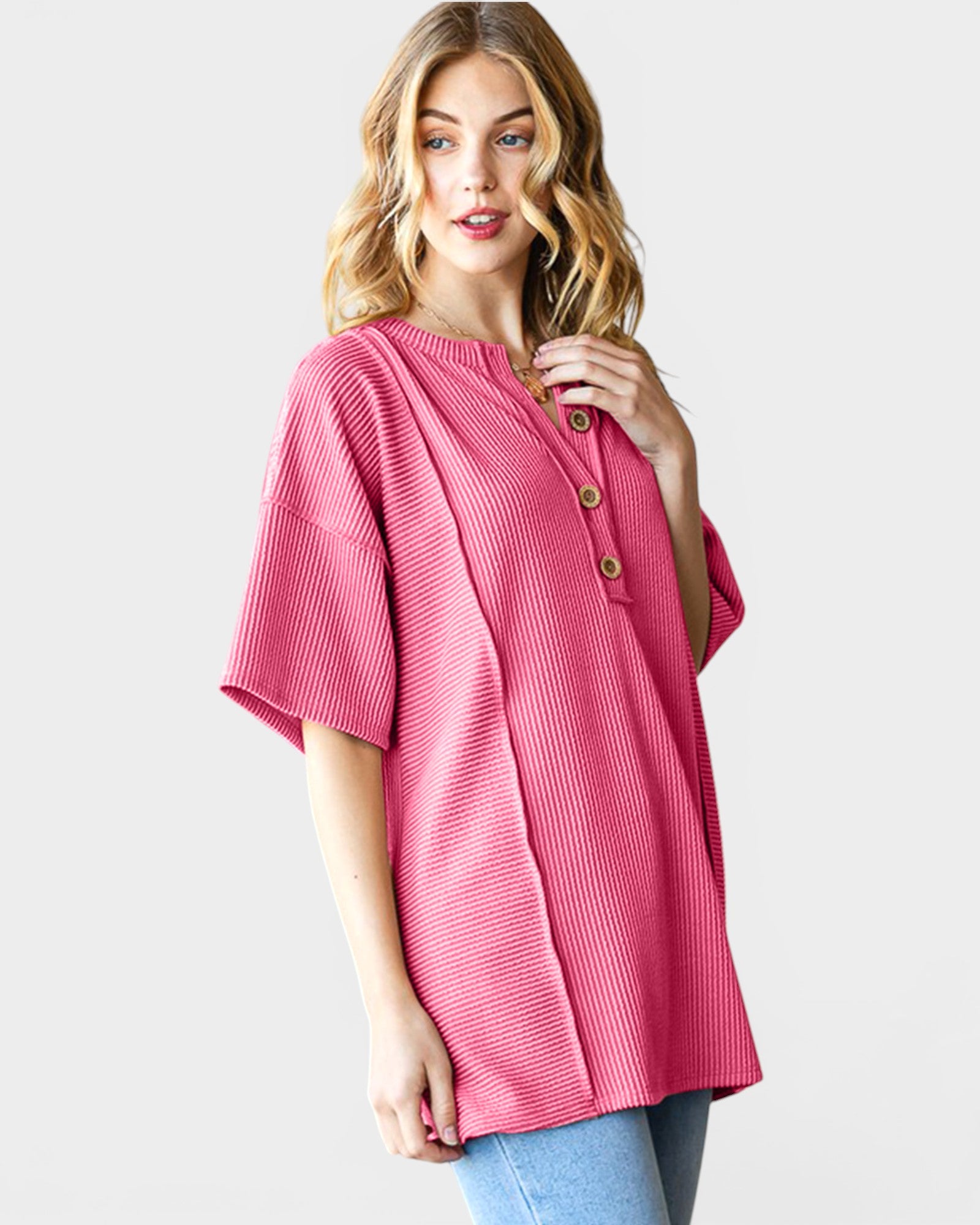 Woman wearing a pink ribbed sweater with button details on a white background