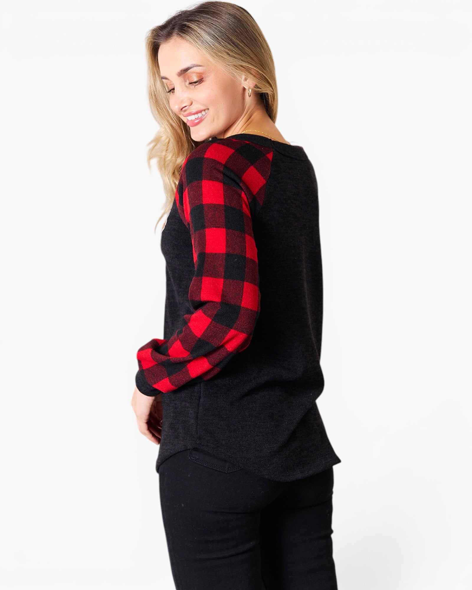 A woman wearing a black knit sweater with red and black buffalo plaid raglan sleeves, shown from a side-back angle against a plain white studio background.
