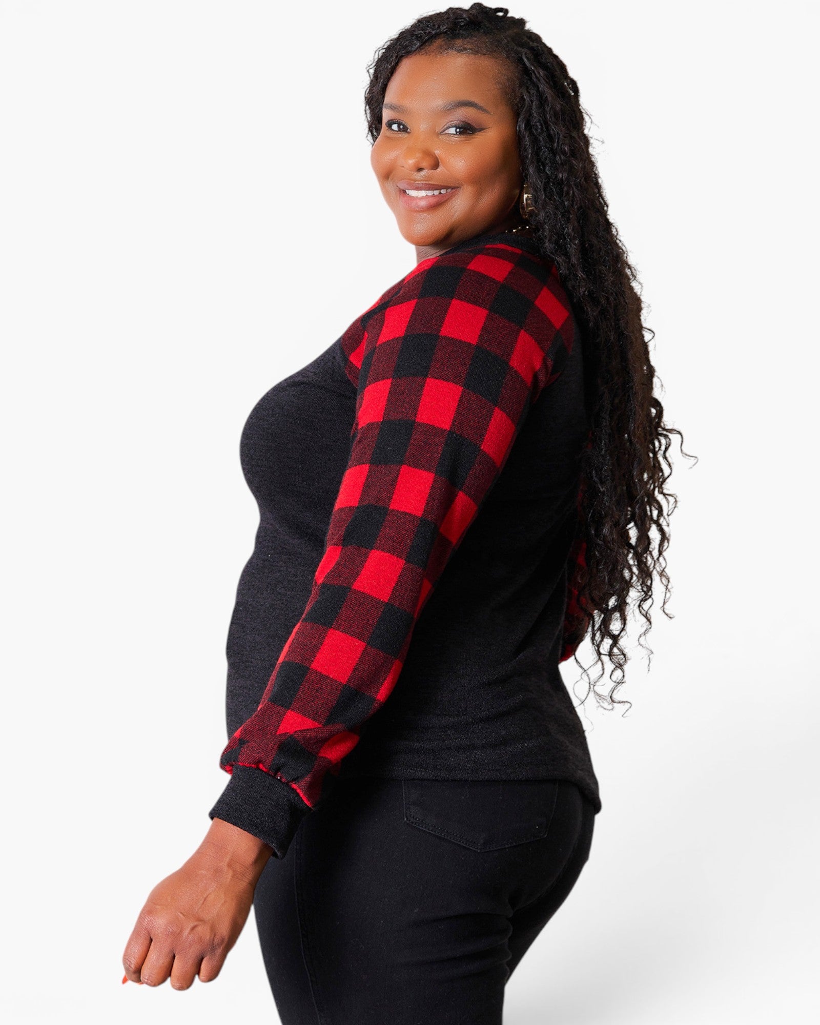 A woman modeling a long-sleeve top with a black body and one red-and-black buffalo plaid sleeve, photographed against a light gray studio background.