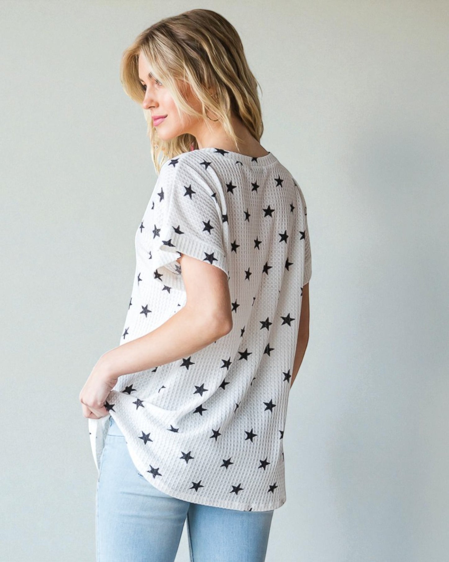 Woman wearing a white t-shirt with black star patterns against a plain background