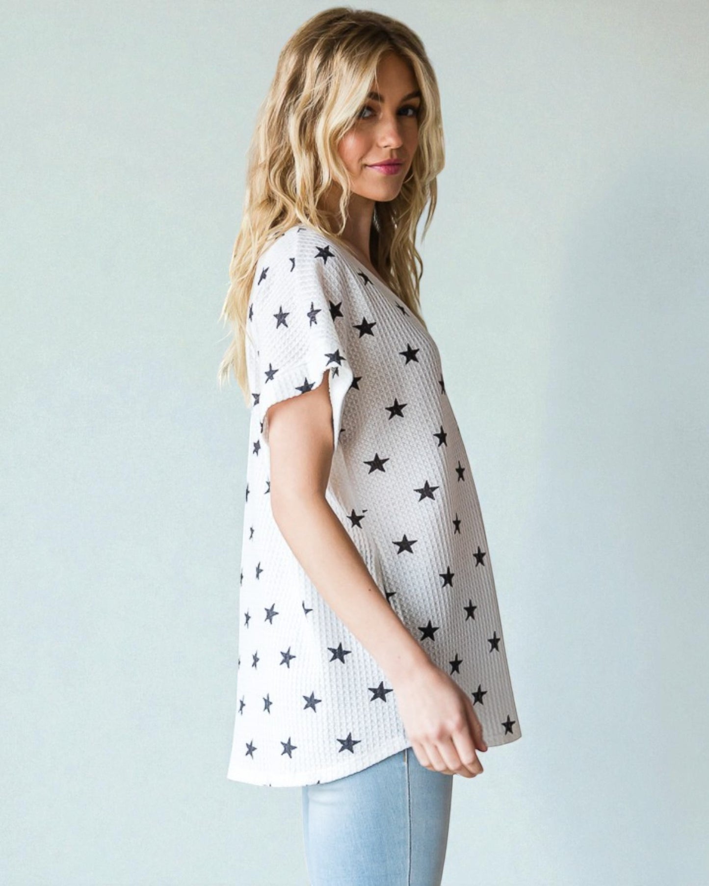 Woman wearing a white top with black star patterns against a plain background