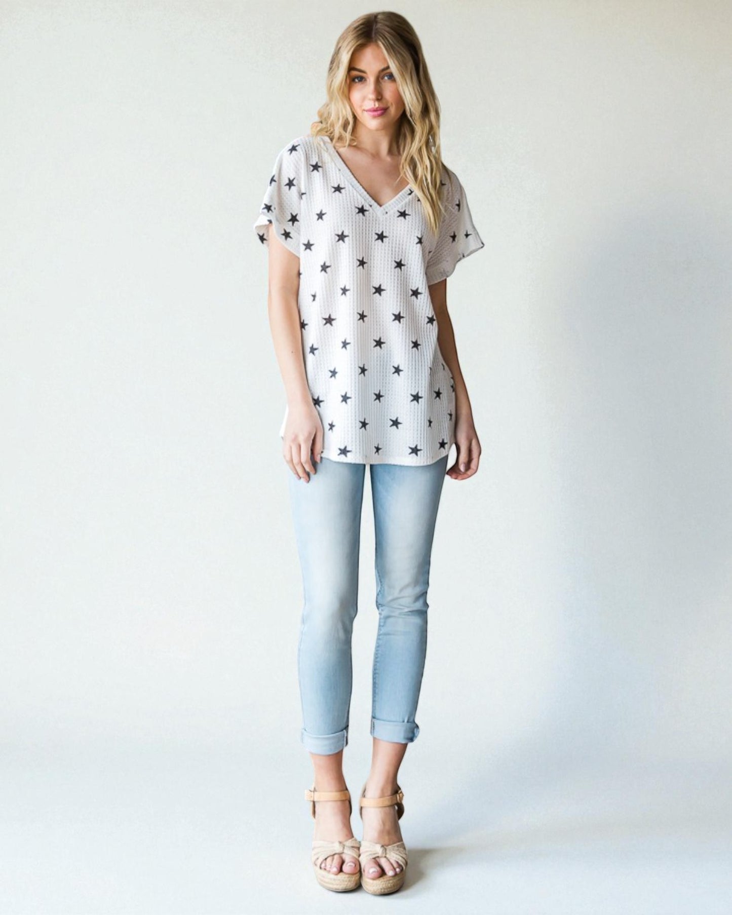 Woman wearing a white star-patterned top and light blue jeans on a plain background