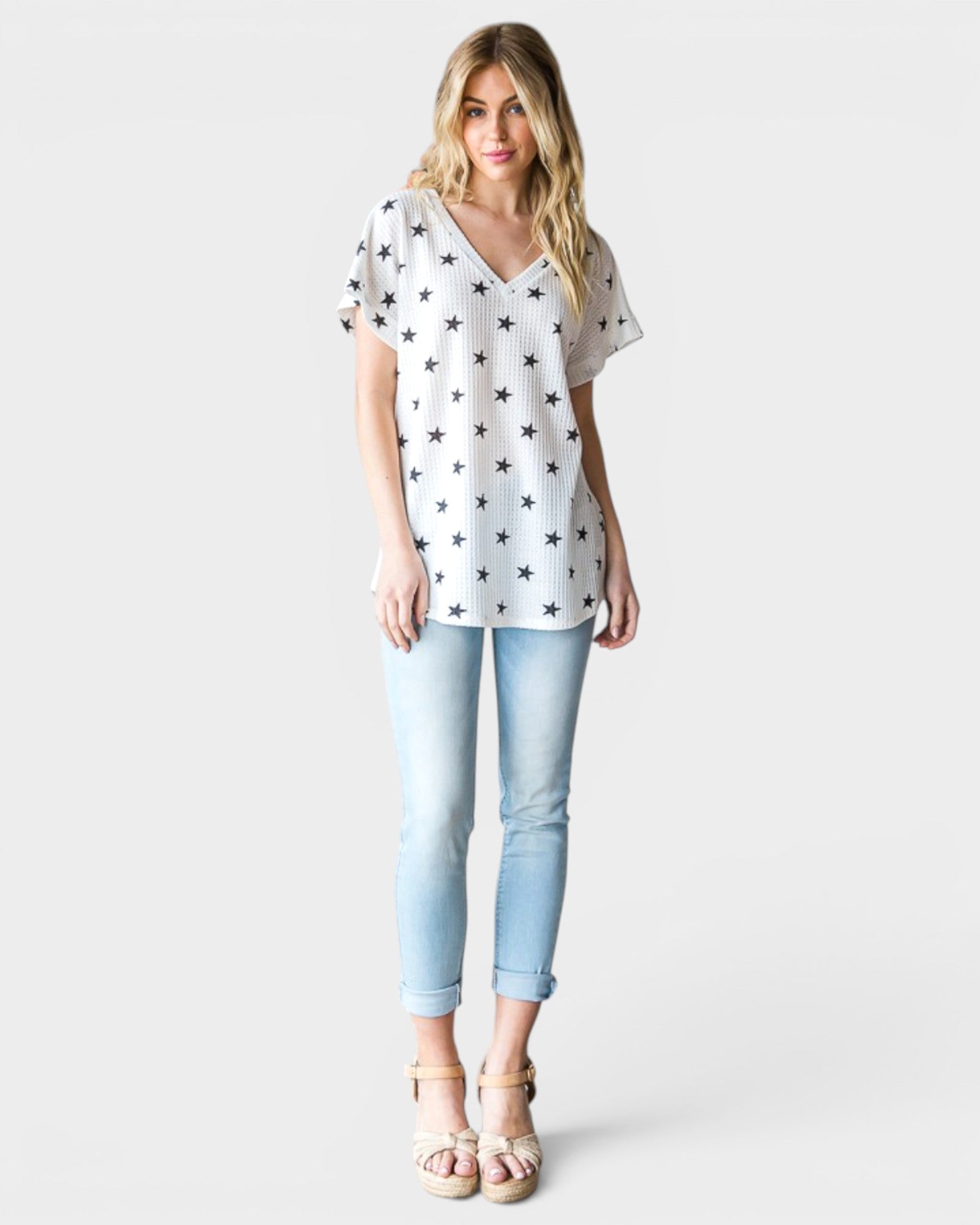 Woman wearing a white star-patterned top and light blue jeans on a white background