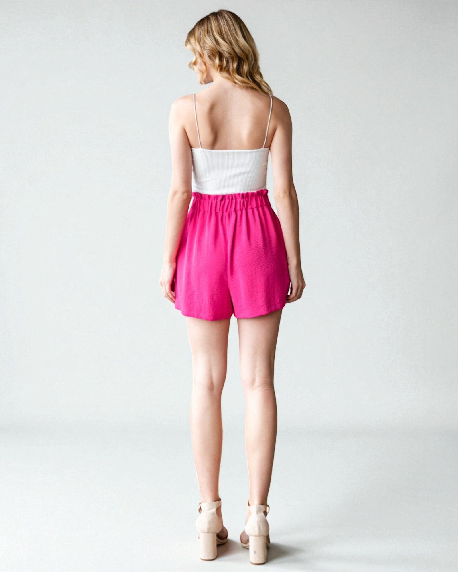 Woman wearing a white top and pink shorts on a plain background