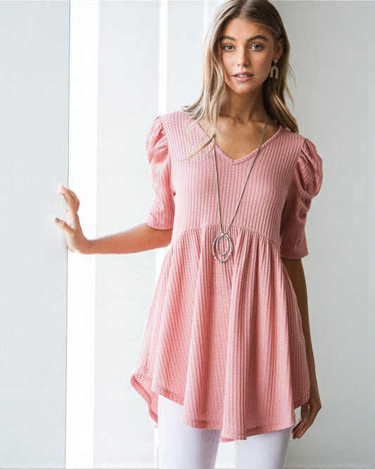 Woman wearing a pink blouse with puff sleeves against a white background