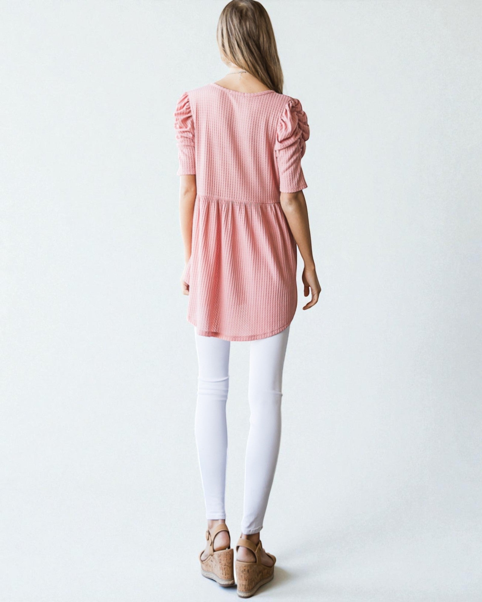 Woman wearing a pink dress with puffed sleeves and white pants on a plain background