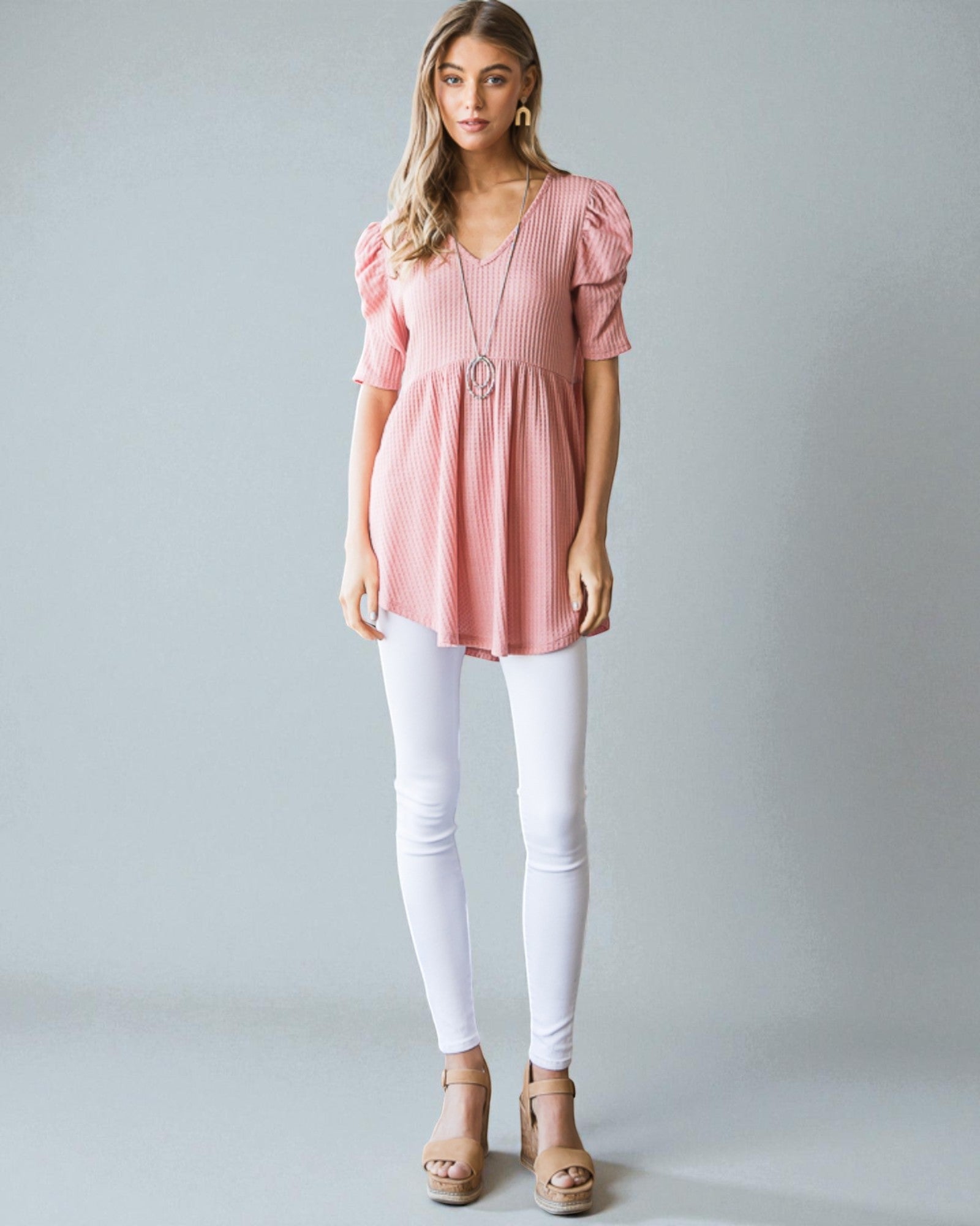 Woman wearing a pink blouse and white pants against a gray background