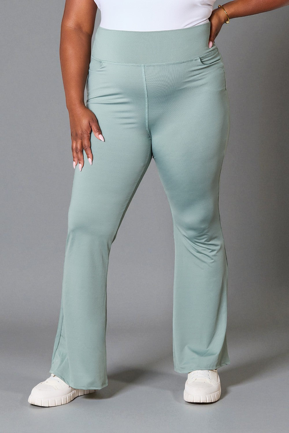 Person wearing light green flared pants on a gray background