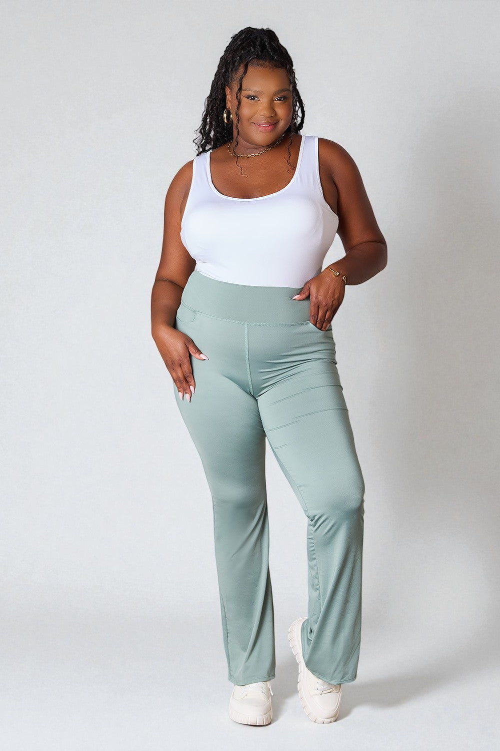 Woman wearing a white tank top and light green pants on a plain background