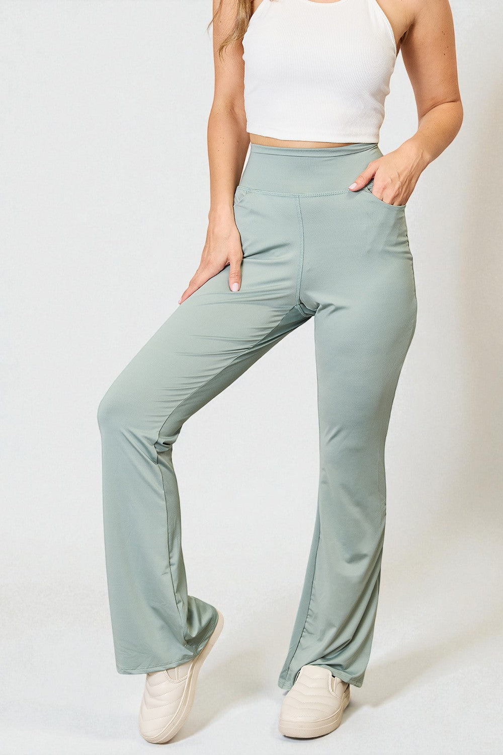 Person wearing light green wide-leg pants and a white top on a plain background