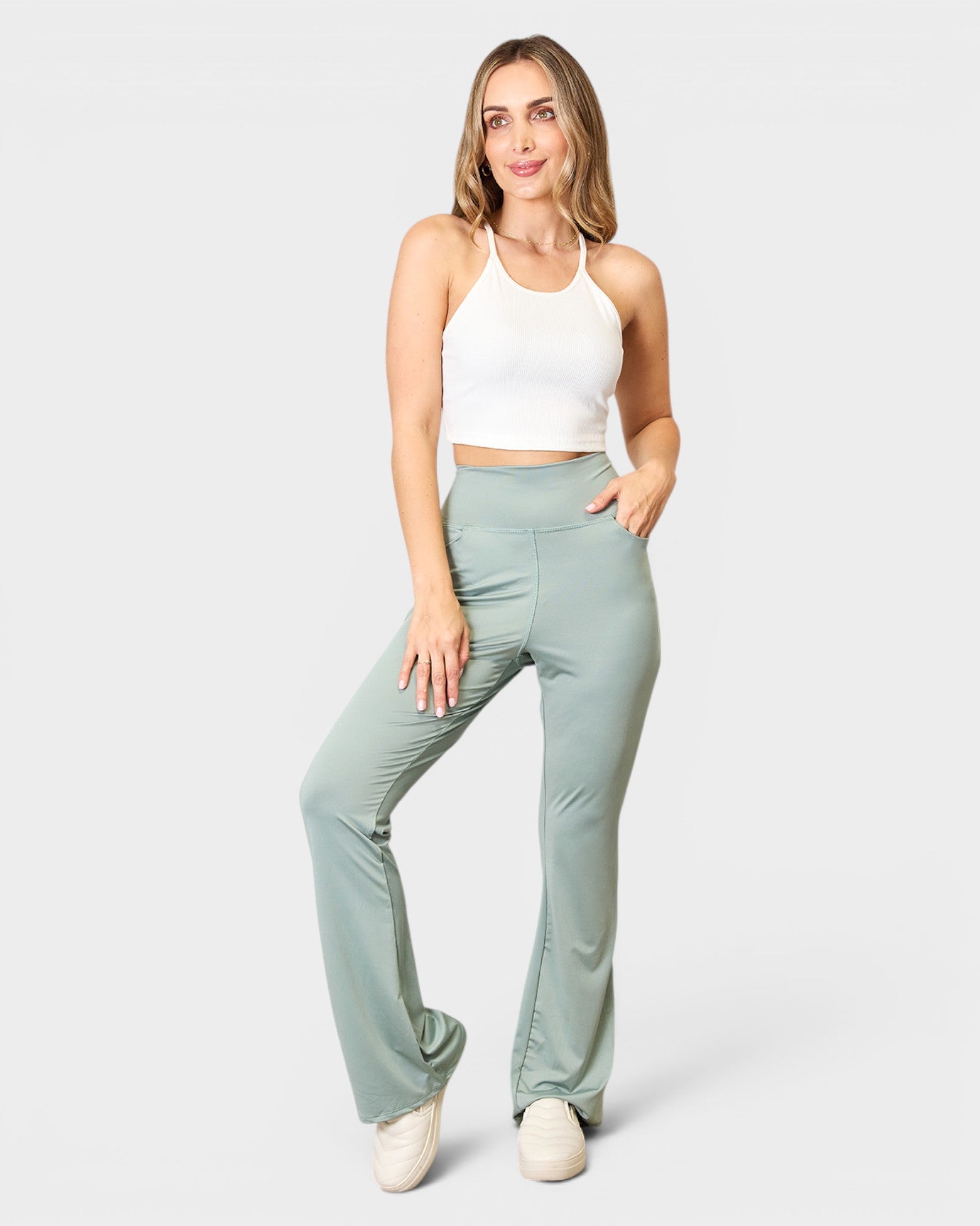 Woman wearing light green pants and a white top on a white background