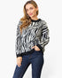 A woman modeling a black and white zebra-print knit sweater with black ribbed trim, paired with dark blue jeans, against a plain white studio background.