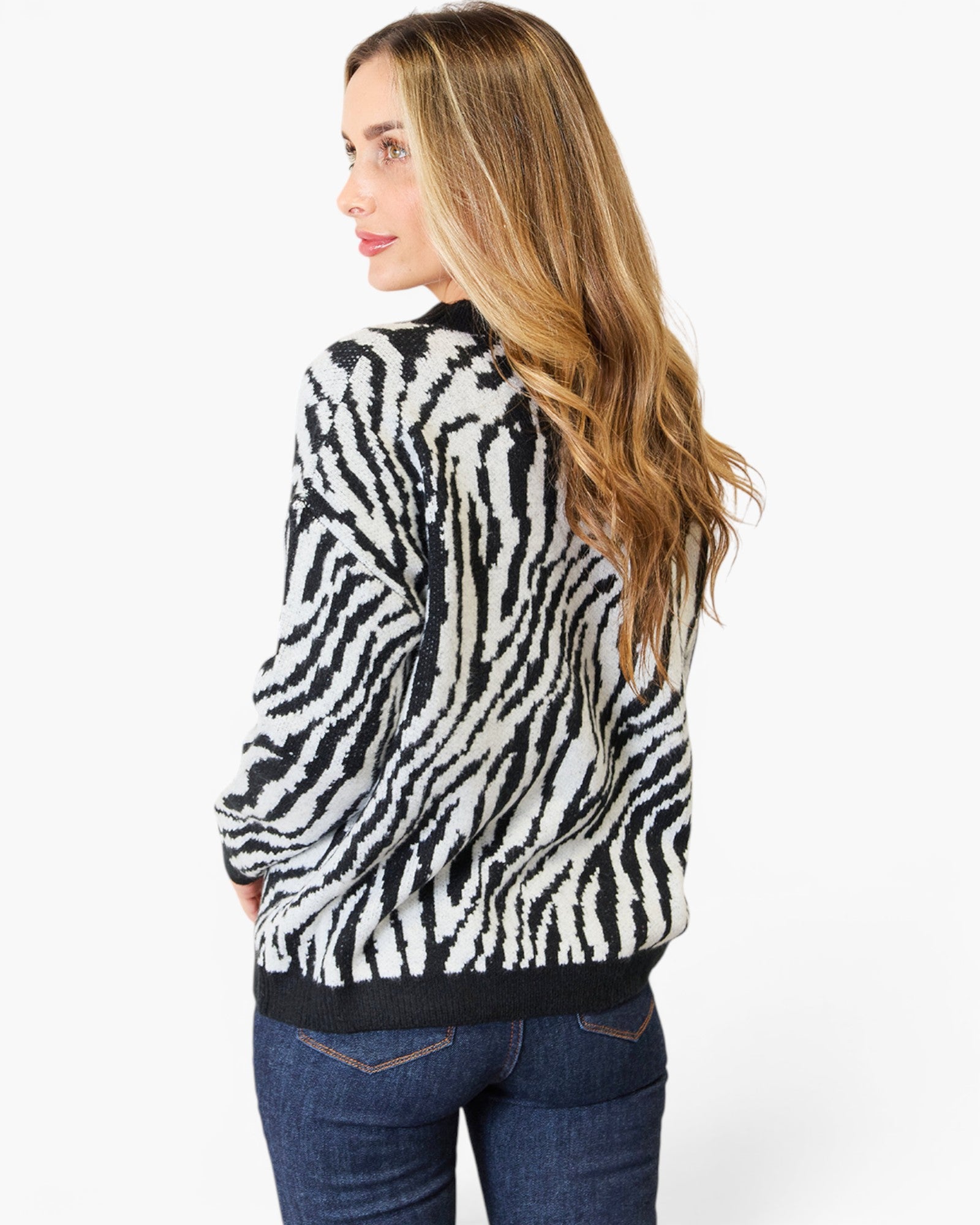A woman with long blonde hair is shown from the back wearing a black and white zebra-print knit sweater and blue jeans against a plain white background.