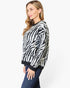 A woman wearing a black and white zebra-patterned knit sweater with dark ribbed trim, paired with dark blue jeans, photographed against a plain light gray studio background.