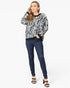 A woman modeling a black and white zebra-print long-sleeve sweater with dark blue skinny jeans and black heeled sandals, standing against a plain white studio background.