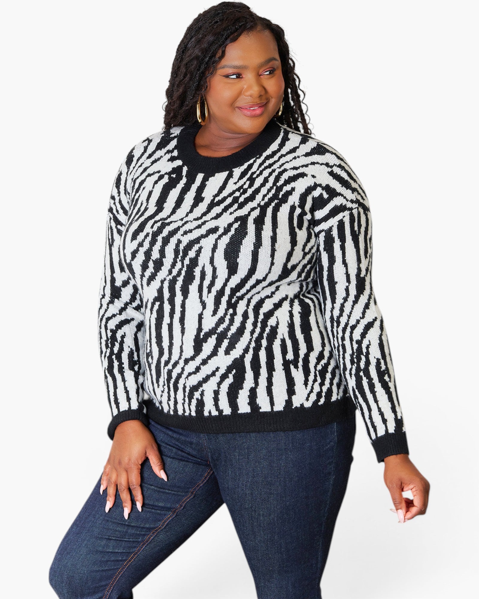 A woman modeling a black and white zebra-print knit sweater with dark blue jeans against a plain white background.