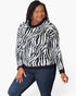 A woman modeling a black and white zebra-print knit sweater with dark blue jeans against a plain white background.