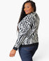 A woman wearing a black and white zebra-print knit cardigan sweater with dark blue jeans, photographed against a clean white studio background.