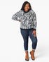 A woman modeling a black and white zebra-print sweater with dark blue jeans and brown ankle boots, standing against a light gray studio background.