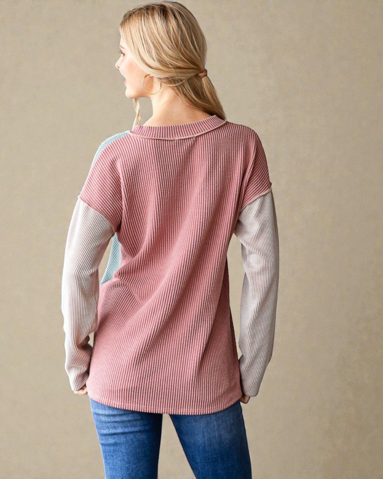 Woman wearing a pink ribbed sweater with long sleeves against a beige background