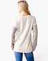 A woman shown from the back wearing a cream ribbed long-sleeve top with sheer pink sleeves and light blue sheer shoulder panels, paired with blue jeans, against a plain white background.