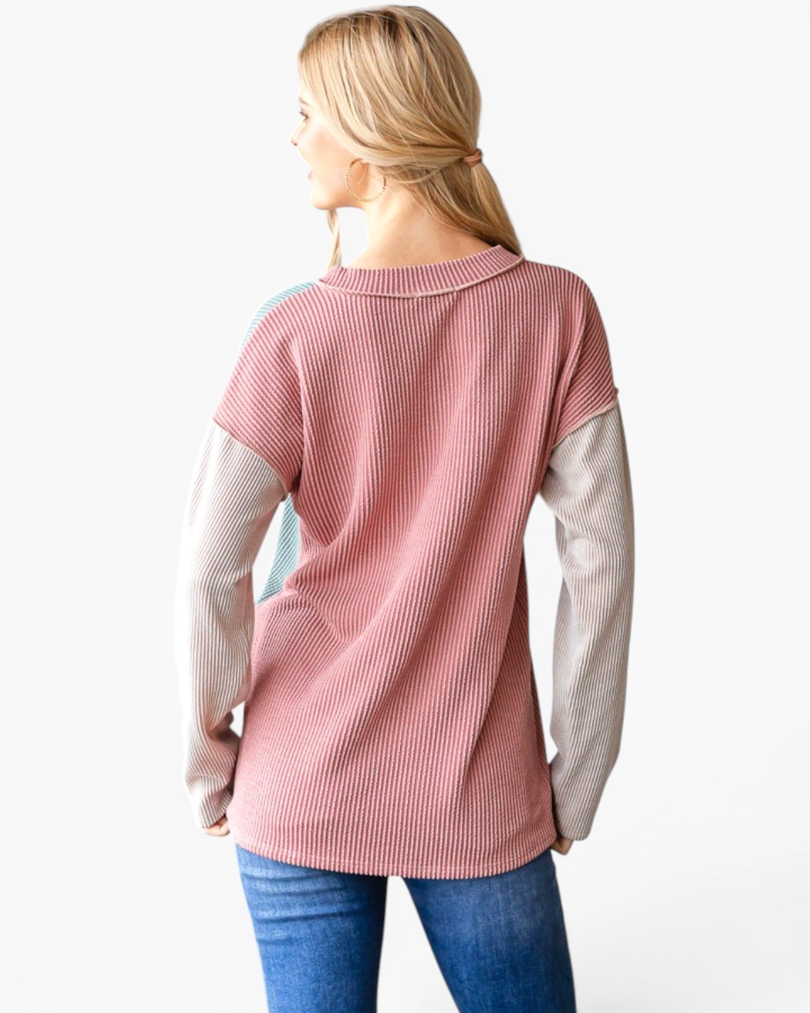 A woman shown from the back wearing a long-sleeve ribbed knit top with a dusty pink body and light beige sleeves, paired with blue jeans against a plain white background.