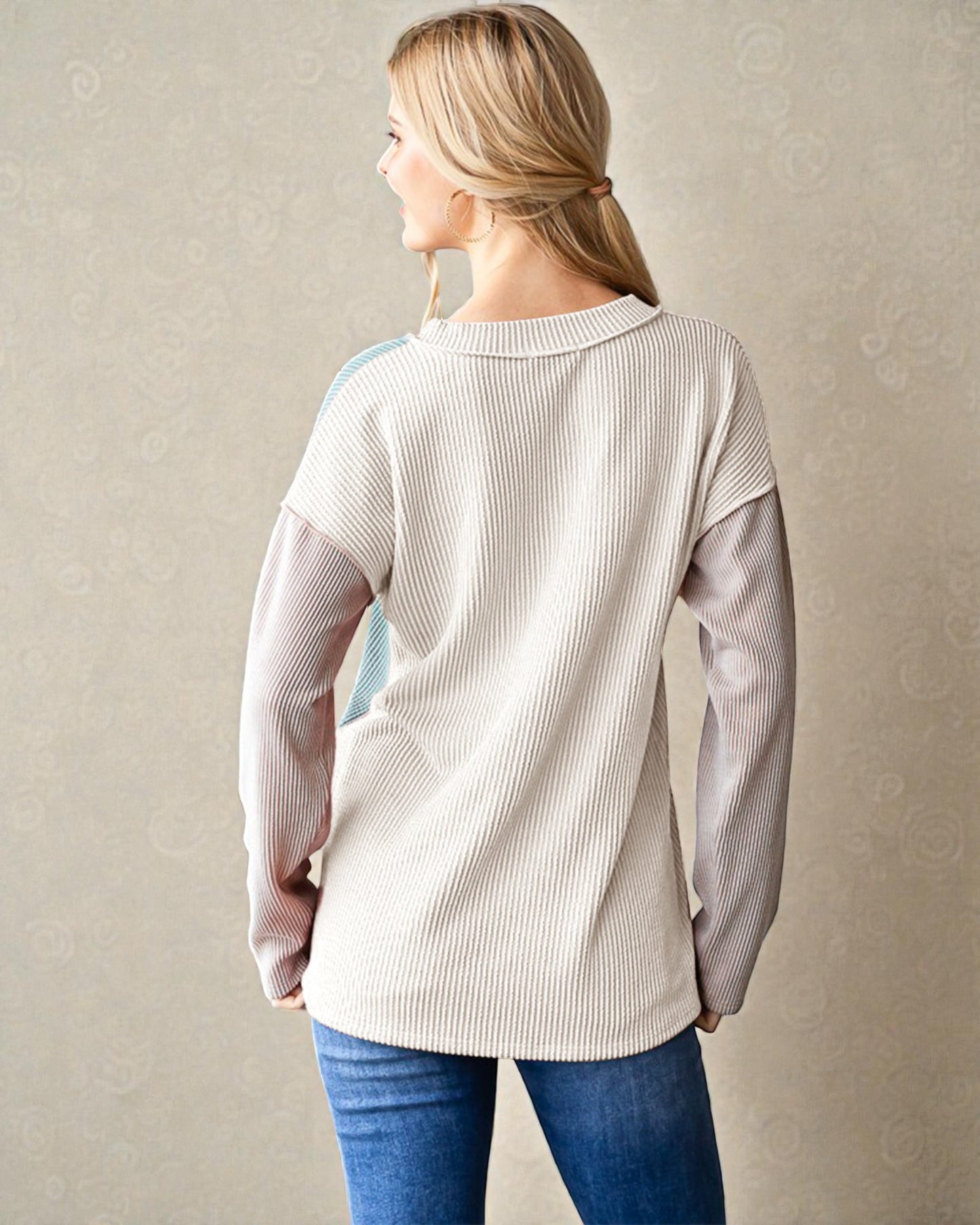 Woman wearing a beige ribbed sweater with a subtle pattern against a plain background