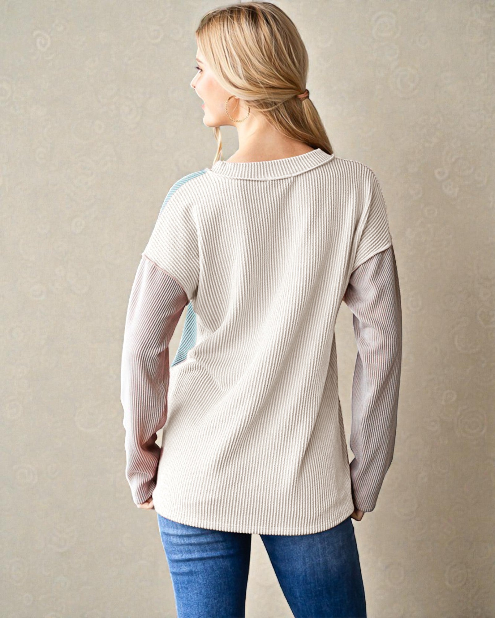 Woman wearing a beige ribbed sweater with a subtle pattern against a plain background